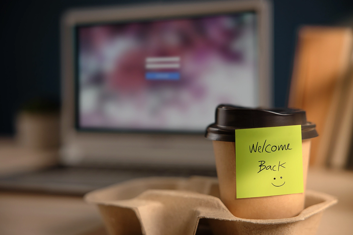 Kaffemugg med texten welcome back med en dator i bakgrunden