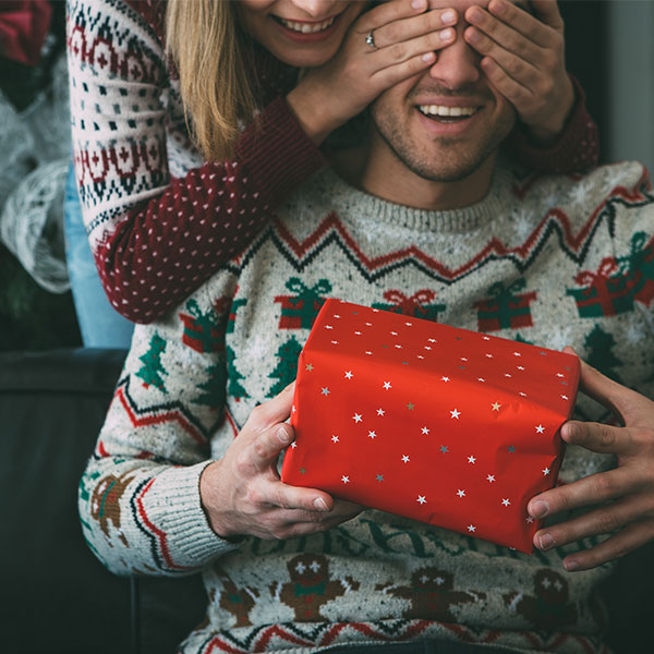 Kvinna håller för ögonen på en man som får en julklapp