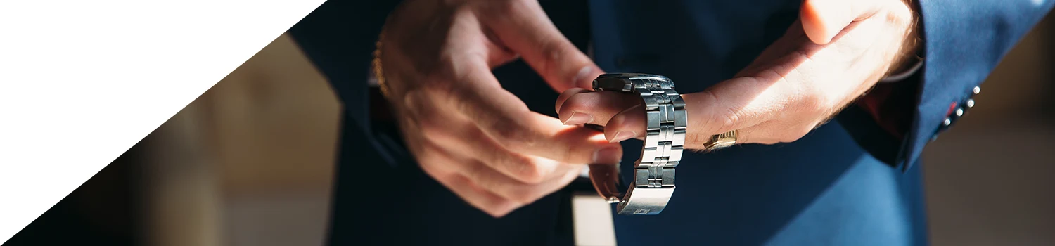 En man i blå kostym håller in en herrklocka med stålarmband