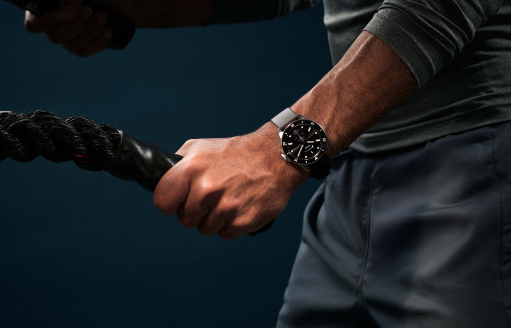 En man iklädd grå träningskläder tränar intensivt med två rep. På handleden sitter en svart smartwatch från Withings – en som kombinerar klassisk design med smart teknik, perfekt för både träning och stil.